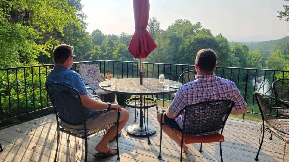 Two men having a discussion looking over a wooded area.