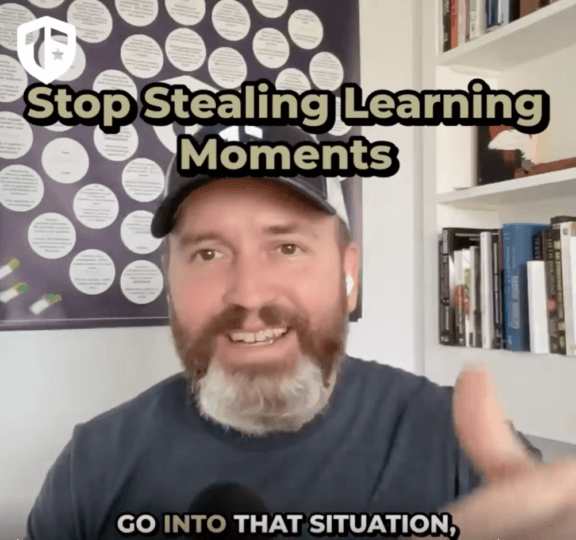 Coach Brandon Jenkins writes about leadership and not stealing learning moments. He is pictured in his office, wearing a grey shirt in his office.