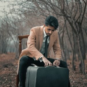 mahdi-bafande-4iPiRmWE0dE-unsplash Man opening suitcase in the woods.