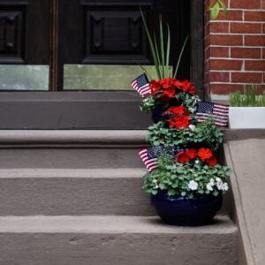 navarjun-singh-CqX8rHuTqoQ-unsplash Porch with ascending steps, with flowers and American flags inside planters.