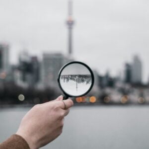 sam-3bxGczE-Axc-unsplash Image is of a magnifying glass, held by a hand, looking at a cityscape. Author Brandon Jenkins writes about uncovering your core.